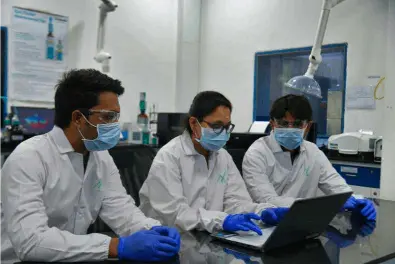Researchers in lab coats and masks working collaboratively on a laptop in a laboratory setting.